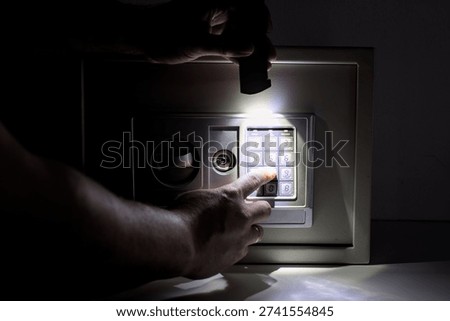 Man entering security code on electronic safe box in dark room with flashlight
