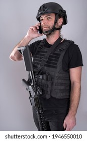 Man Equipped For Airsoft With Helmet And Protective Vest Is Confirming The Negociation Strategy On The Phone While Standing With His Weapon Displayed