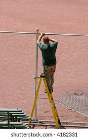 A Man Erecting A Chain Link Fence In A Park