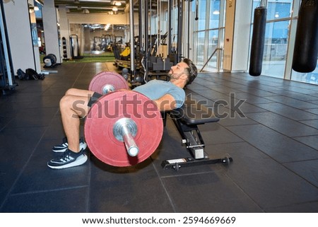 Man executing a barbell hip thrust on a bench in a modern gym setting, focusing on strength training and fitness routines