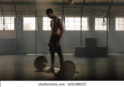 Man exercising with barbell at gym. Man standing with heavy weights barbell on gym floor.