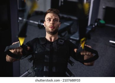 A man exercising in the gym on TRX straps. A photo of a young sexy man with special EMS equipment and in good physical shape in an isolated indoor gym. New sports technologies, the training revolution