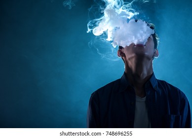 man exhales thick smoke on blue background