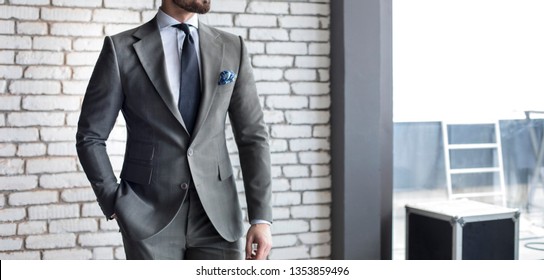Man in expensive custom tailored suit standing and posing indoors in front of brick wall background 