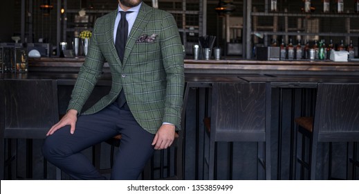 Man in expensive custom tailored suit with green jacket sitting and posing at bar