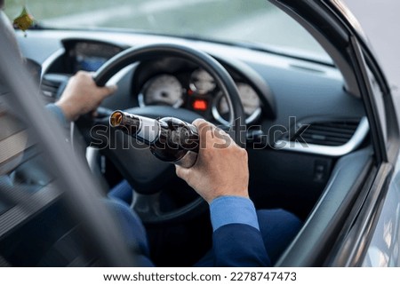 A man in an expensive suit drinks beer at the wheel of a car causing the danger of an emergency. A businessman drinks while driving. Drunk driver concept