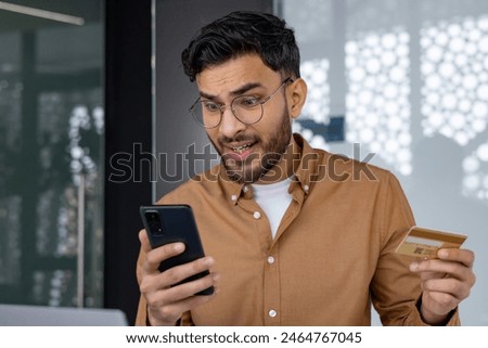 Man experiencing frustration while checking credit card transaction on smartphone. Concept of online shopping, financial problem, or fraud.