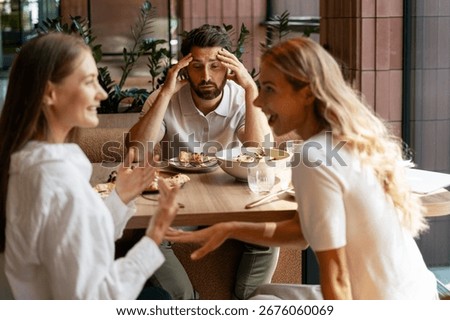 Man experiencing a headache while enduring loud women arguing during a business lunch at a restaurant table