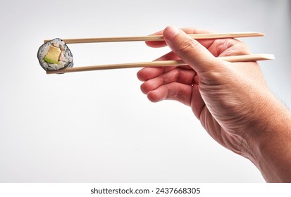 A man expertly grips a sushi roll with chopsticks against a white background, highlighting japanese cuisine and dexterity. - Powered by Shutterstock