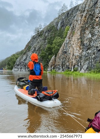 A man expertly pulls a vibrant and brightcolored kayak down a tranquil and serene river, skillfully aided by the gentle current, surrounded by picturesque beautiful nature and an expansive blue sky