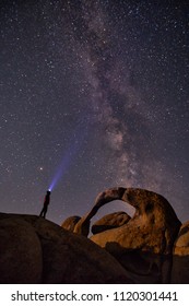 Man Exploring Mobius Arch At Night Under The Milky Way Galaxy At Alabama Hills, Lone Pine, California, USA