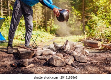 Man extinguishing campfire with water from cauldron in summer forest. Put out campfire by tent. Traveling fire safety rules