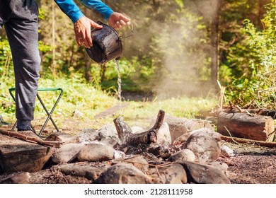 Man extinguishing campfire with water from cauldron in summer forest. Put out campfire by tent. Traveling fire safety rules