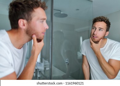 Man Face Care Looking In Mirror Touching His Beard Or Skin Health. Male Beauty Morning Skincare Routine In Home Bathroom. After Shave Men Lifestyle Concept.