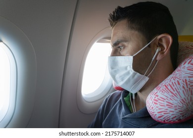 Man With Face Mask, Earphones And Neck Pillow Looking Through Plane Window. Airplane Health Protection Measures, Long Trip Comfort Concepts