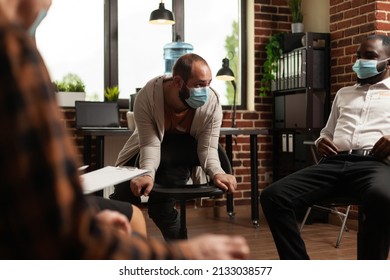 Man With Face Mask Talking To Group At Aa Meeting Program About Health Issues. Multi Ethnic People With Addiction Attending Therapy Session And Having Discussion About Problems.