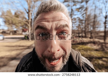 man, face, portrait, closeup, expression, angry, funny, emotion, distorted, wideangle, beard, adult, male, human, outdoor, park, humor, exaggerated, eyes, nose, wrinkles, skin, detail, candid, lifestyle, character, intense, dramatic, quirky, playful, expressionism