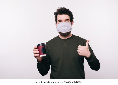 man with facial mask holding cup of coffee and showing thumbs up over white background - Powered by Shutterstock