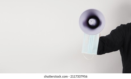 The Man Facing Straight Is Holding A Megaphone And Face Mask And He Wears A Black Shirt On White Background. Studio Shooting.