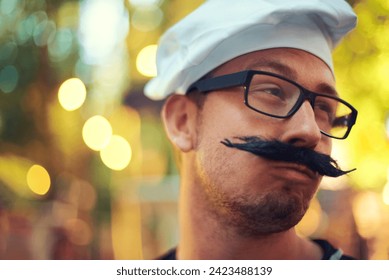 Man, fake mustache and beret in chef costume with comic face, creative and confident in french baking. Young person, glasses and cooking job in bokeh and culinary education in pastry art in europe - Powered by Shutterstock