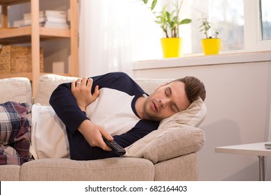 Man Falling Asleep At Home While Watching TV. Lazy Freelancer Lying On Sofa During Working Hours.