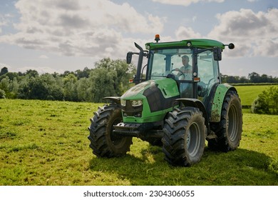Man, farm and green tractor on grass in countryside for agriculture, lawn or sustainability in nature. Male person or farmer in big agricultural machinery for farming, ecology or construction on land - Shutterstock ID 2304306055