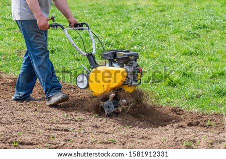 Man Farmer plows the land with a cultivator. Agricultural machinery: cultivator for tillage in the garden,motor cultivator.