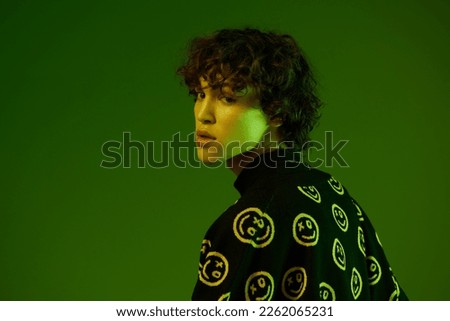 Man fashion and style accessories model with curly hair stylish sweater, hipster teen lifestyle, portrait green background mixed neon light, copy space