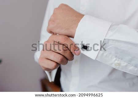Man fastening a cuff-link on the shirt. Groom fastens cufflinks on the shirt