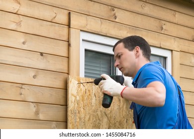 A Man Fastens A Plywood Sheet To Protect The Windows From Natural Disasters