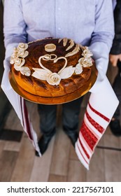 A Man, A Father, Holds A Round Loaf Decorated With Flowers, A Swan With An Embroidered Towel In His Hands. Close-up Wedding Food Photography.