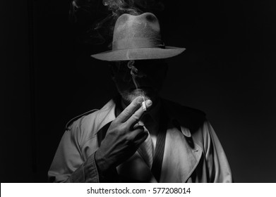 Man With Fedora Hat And Trench Coat Smoking A Cigarette In The Dark, 1950s Noir Film Character