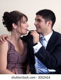 man feeding woman chocolate; both are dressed in formal attire as if attending a dinner party or similar event.