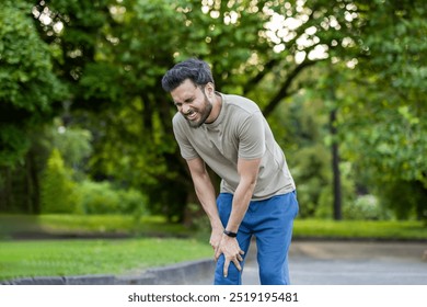 Man feeling knee pain during fitness exercises in nature setting. Concept of outdoor workout challenges, physical discomfort, pursuit of health and wellness in park environment. - Powered by Shutterstock