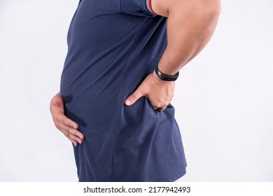 A man feeling lower back pain in the lumbar region. Suffering from a bulging or ruptured disk. Stretching to mitigate and alleviate the symptoms. Isolated on a white backdrop. - Shutterstock ID 2177942493
