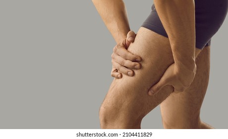 Man feeling pain or having thigh cramp. Sportsman who's suffering from hamstring muscles pain after running, jogging or gym fitness training standing on grey copy space background and touching his leg - Shutterstock ID 2104411829