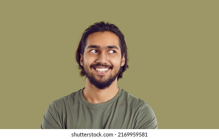 Man feels uncomfortable and looks to side. Head shot bearded mustached South Asian guy experiencing awkward moment. Funny guy likes something, admires someone, casts secret glance sideways and smiles
