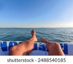 man feet sitting on inflatable boat over the sea. Holiday concept. man feet relaxing on beach, enjoying sun and splendid view. barefoot sunbathing on summer beach. Happy on holidays vacation concept.