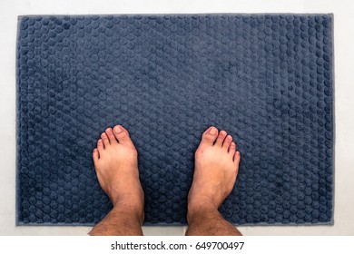 A Man Feet Standing On Gray Bathroom Rug. Top View.