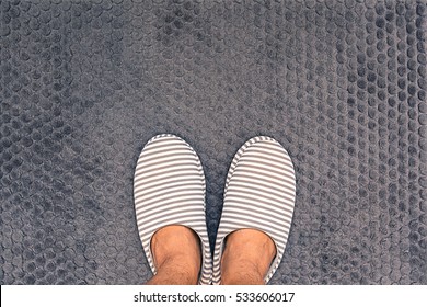 A Man Feet Ware White And Gray Strip Color Slippers On Gray Bathroom Rug. Top View