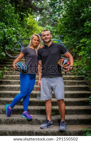 Man and female posing in nature park and holding bicycles helmets.