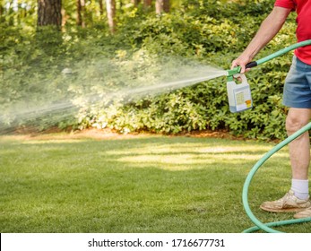 Man fertilizing residential backyard lawn with liquid chemical spreader. Landscaper spraying grass lawn with fertilizer, weed killer, and insecticide.