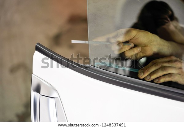 Man filing the edge of a car tinted\
window.Professional car window tinting\
services.