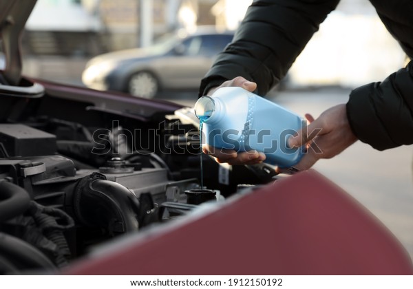 Man filling car radiator with antifreeze\
outdoors, closeup