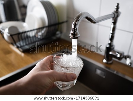 man filling a glass of water from a stainless steel kitchen tap. potable water and safe to drink. male's hand pouring water into the glass from chrome faucet to drink running water with air bubbles.