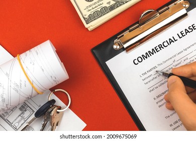 Man Filling Out Commercial Lease Agreement. Clipboard With Business Document, House Keys, Pen And Money. Red Background, Copy Space 