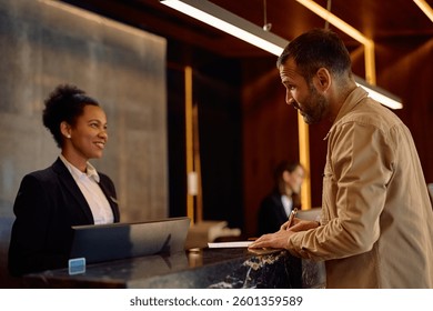 Man filling out documents while talking receptionist and checking in at the hotel.