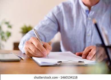 Man filling out a questionnaire on a wooden table. Horizontal composition. Front view.