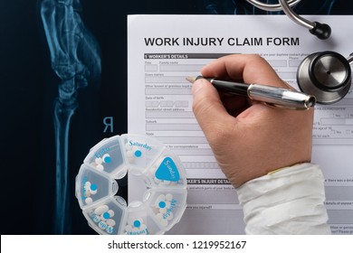 man filling work injury claim form with stethoscope  and box of pills on top of an X-ray film medical and insurance concept