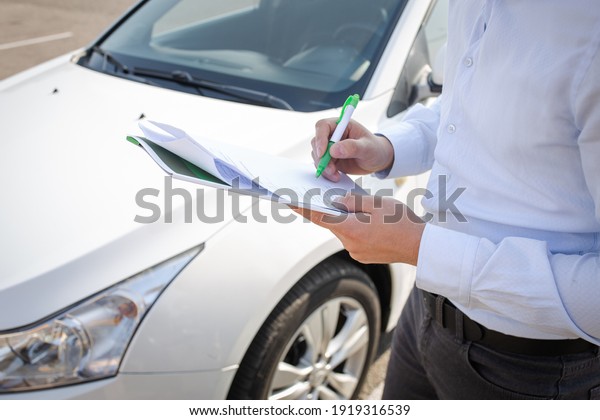 Man\
fills out documents on the background of the\
car